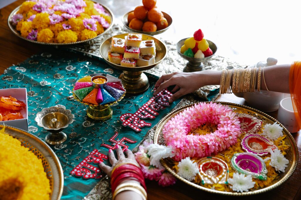 Colorful Indian festival setup with flowers, sweets, traditional decorations, and hands adorned with bangles.